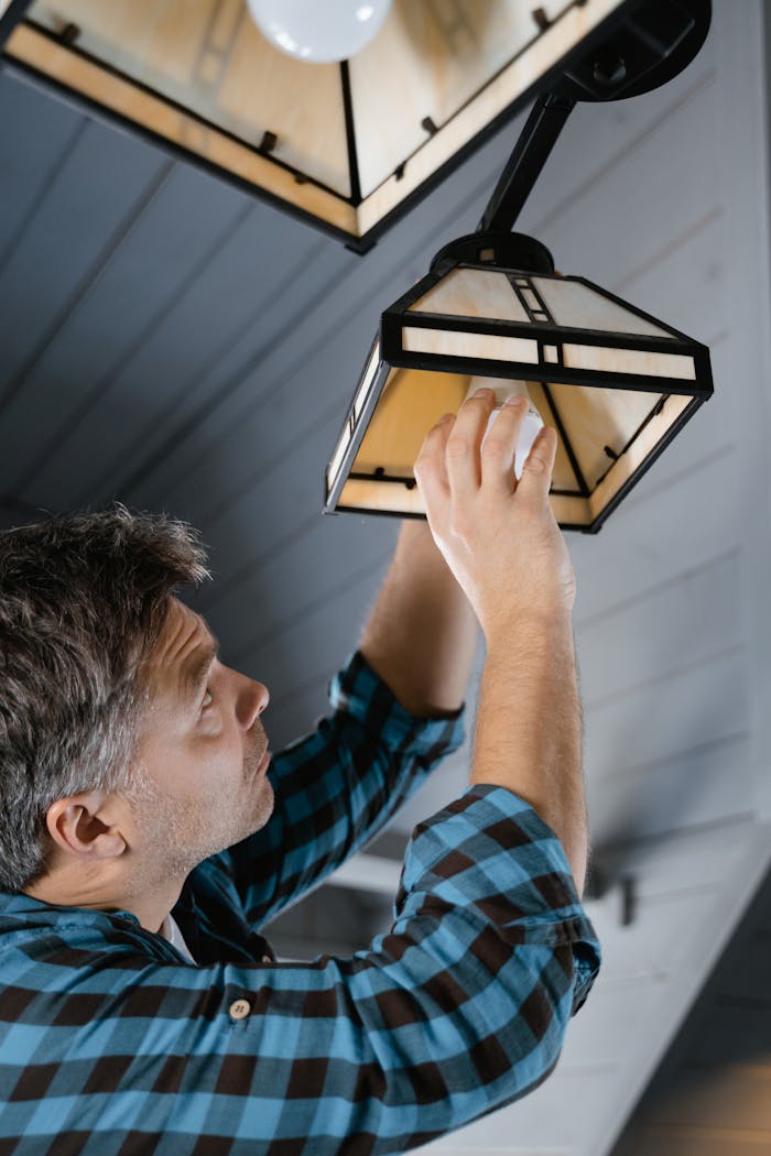 Services Man in plaid shirt fixing a pendant light indoors.